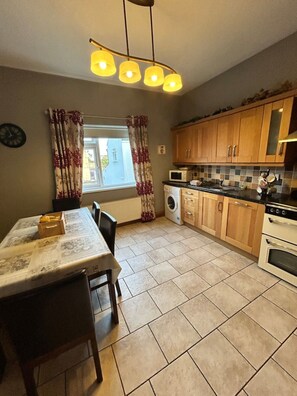 A kitchen with wooden cabinets, a microwave, a washing machine, and a dining table with chairs. - Greencastle – 4-Bed Townhouse Sleeps 8 | Free Parking | Mourne Mountains (Kilkeel)