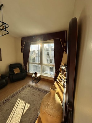 A living room with a sofa, a chair, a large vase, and a view of a building through the window. - Greencastle – 4-Bed Townhouse Sleeps 8 | Free Parking | Mourne Mountains (Kilkeel)