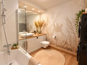 Ein modernes Badezimmer mit einer Badewanne, einem großen Spiegel, einer Toilette und einer Dusche.