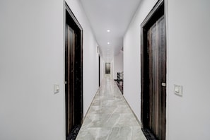 A corridor with white walls, dark wooden doors, and a marble floor leading to a staircase.