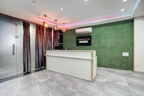 A reception area with a reception desk, a wall-mounted air conditioning unit, and a sign indicating it is serviced by OYO.