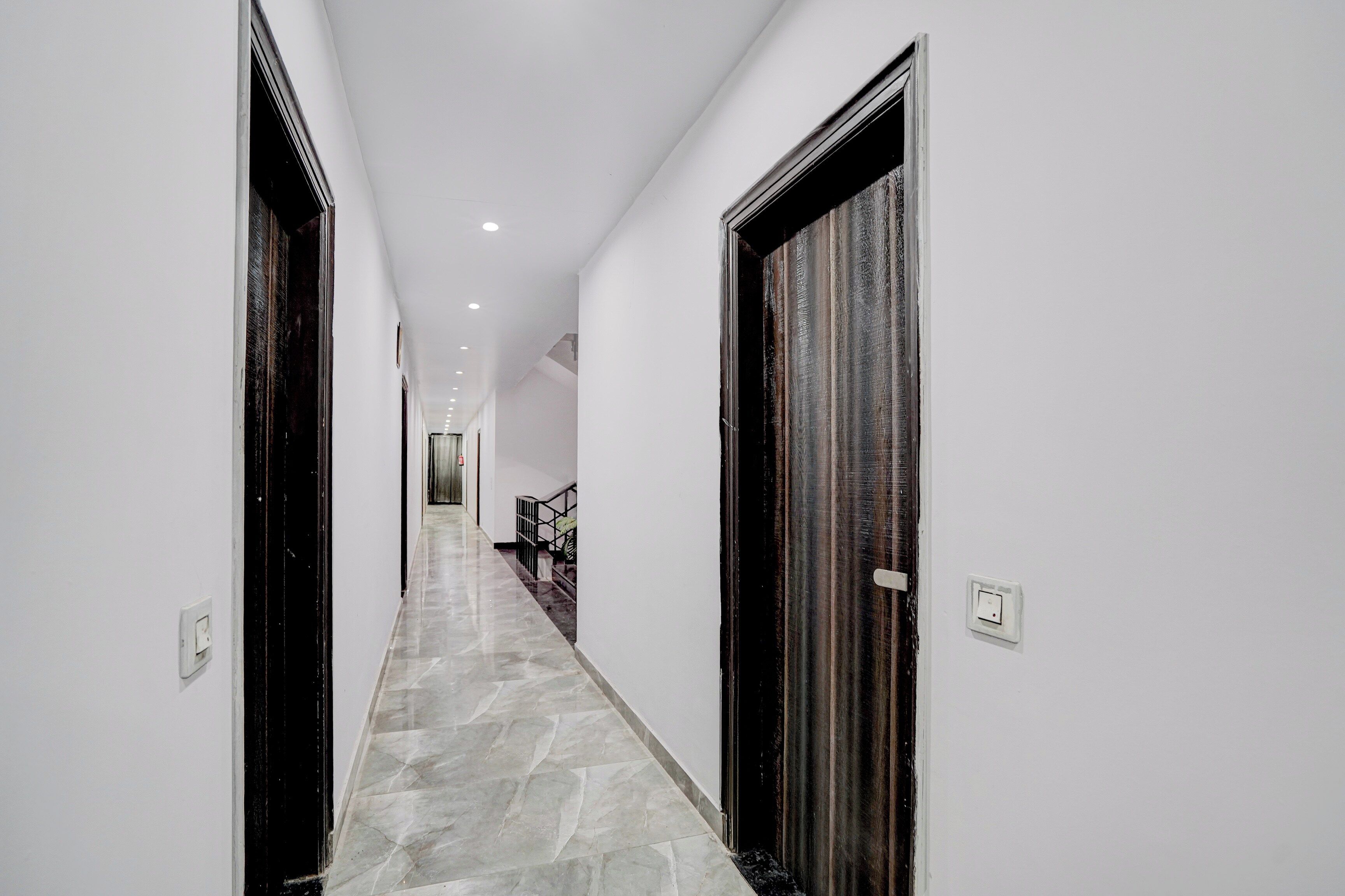 A corridor with a marble floor, white walls, and dark wooden doors.