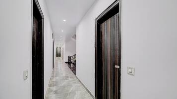 A corridor with a marble floor, white walls, and dark wooden doors.