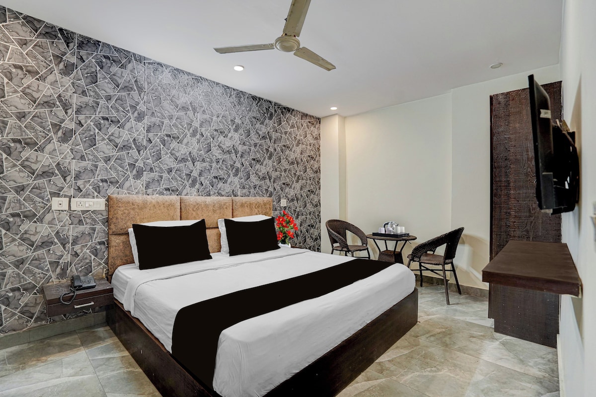 A hotel room with a bed, a desk, chairs, a ceiling fan, and a TV.
