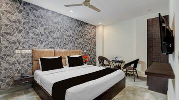 A hotel room with a bed, a desk, chairs, a ceiling fan, and a TV.