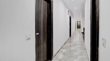 A corridor with white walls and dark wooden doors, leading to a room with a large window.