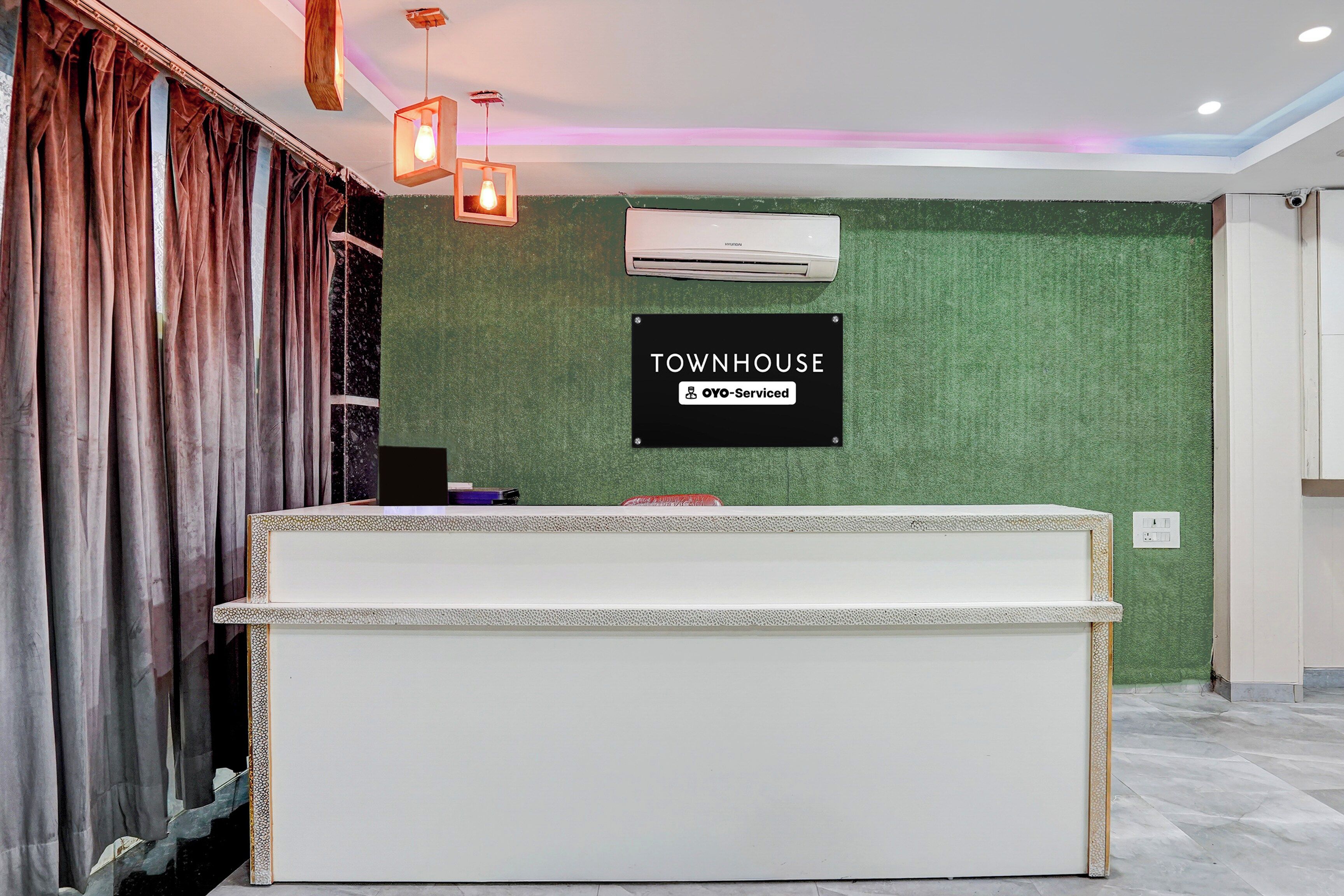 Un mostrador de recepción con un letrero que dice 'TOWNHOUSE OYO-Serviced' frente a una pared verde.