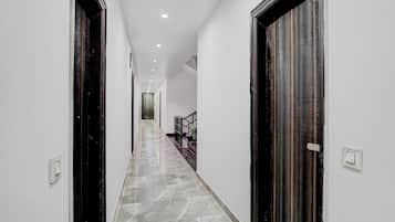 Un pasillo con piso de mármol, paredes blancas y puertas de madera oscura.