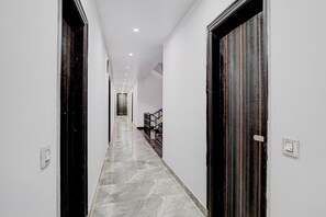 A hallway with a marble floor, white walls, and dark wooden doors.