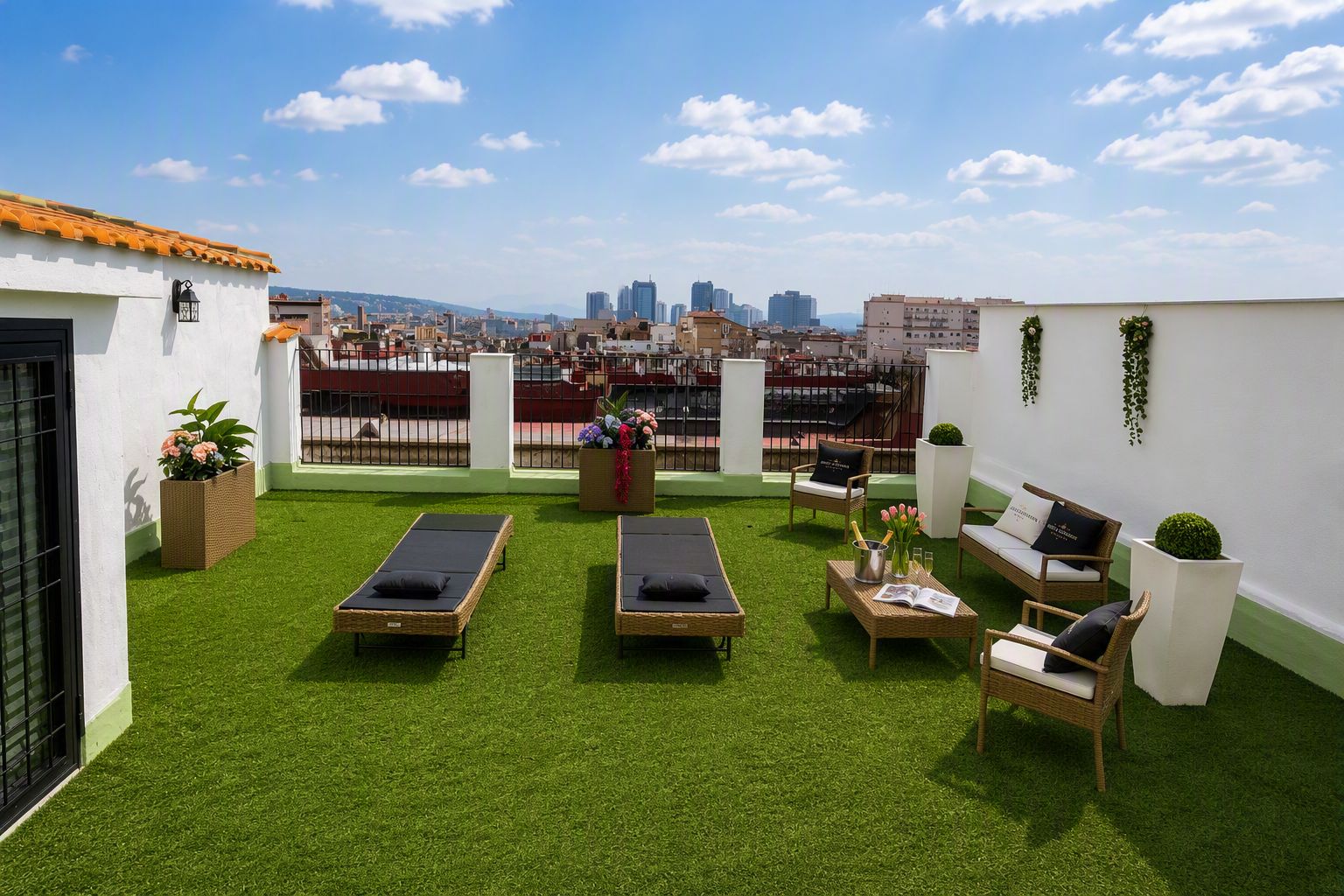 Una terraza en la azotea con césped artificial, dos tumbonas, un sofá y una pequeña mesa con bebidas.