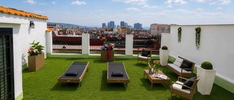 Una terraza en la azotea con césped artificial, dos tumbonas, un sofá y una pequeña mesa con bebidas.