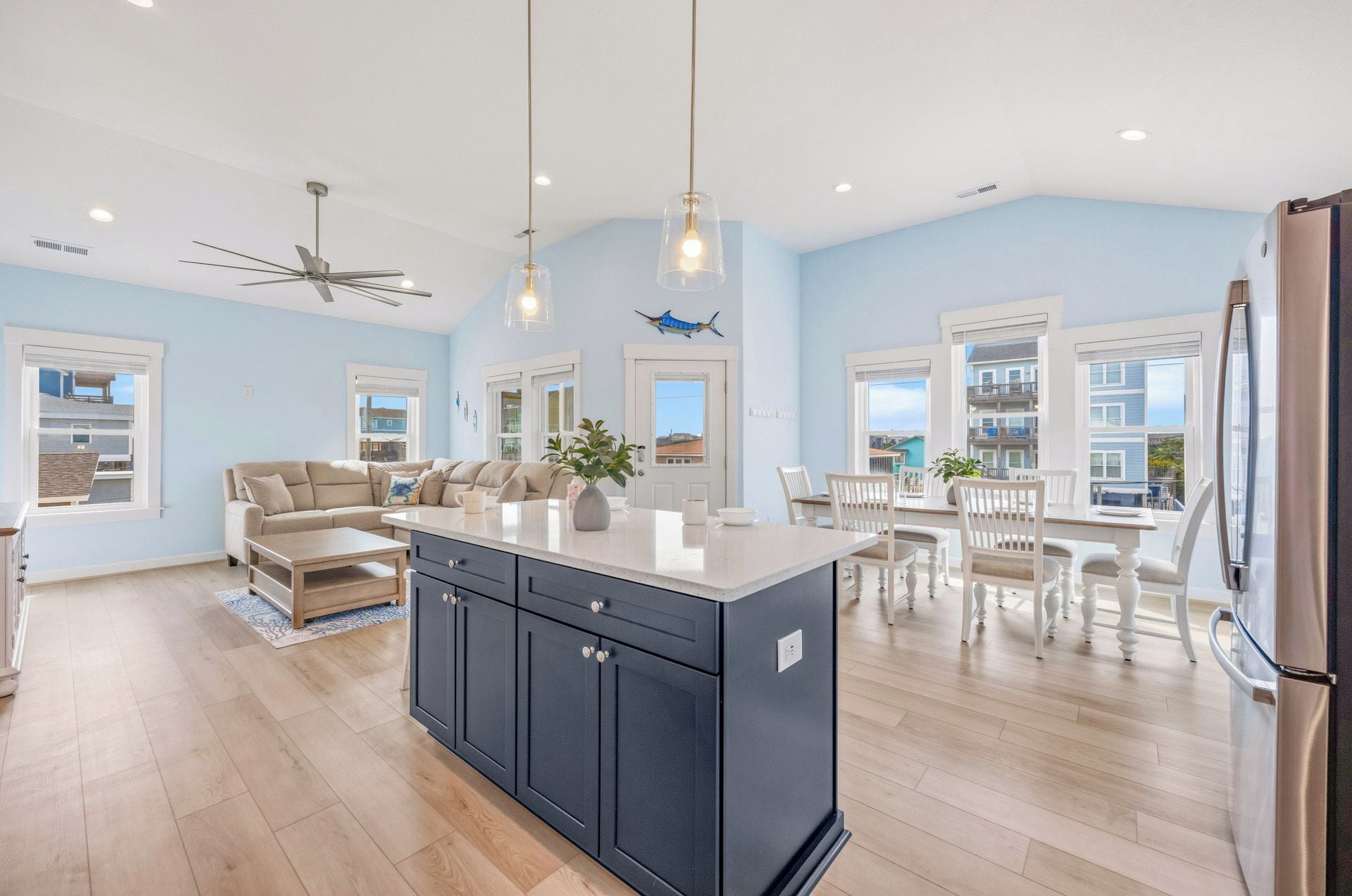 A spacious kitchen with a central island, a dining area with white chairs, and a ceiling fan.