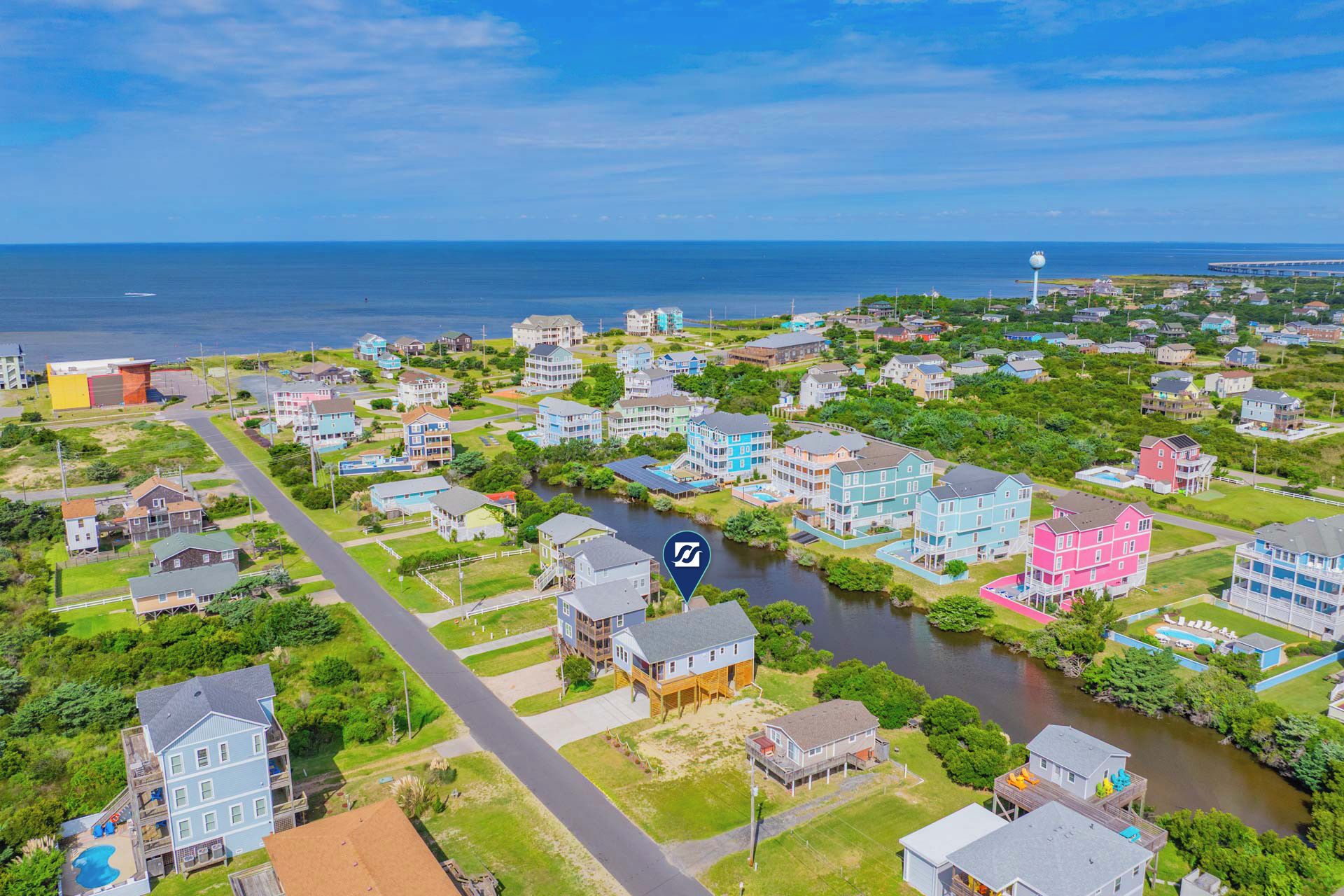 A residential area with houses along a river, a bridge, and a lighthouse in the distance.
