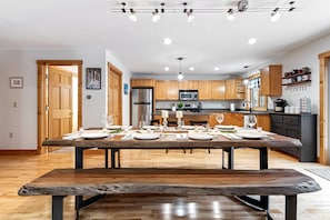 A modern kitchen with wooden cabinets, a stainless steel refrigerator, and a dining area set for a meal. - Stay at the Ski Hive close to Sunday River (Newy)