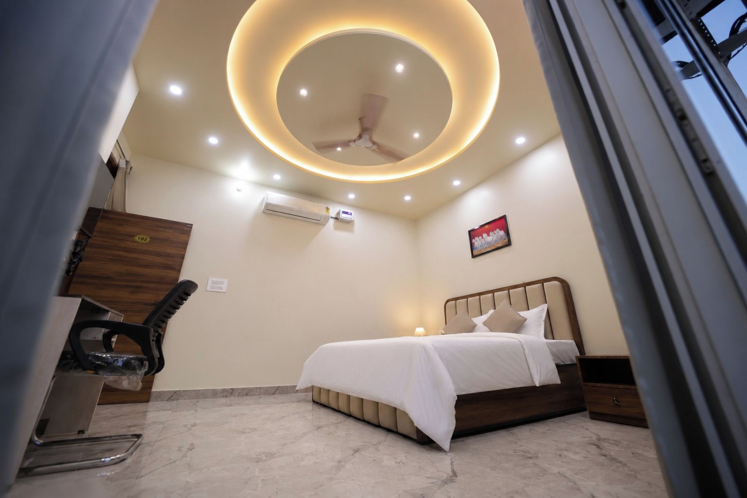 A hotel room with a bed, a desk, an air conditioning unit, and a ceiling fan.