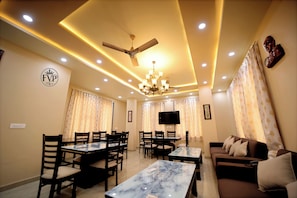 A modern living room with a dining area, featuring a chandelier, ceiling fan, and a flat-screen TV. - Fort View Paradise (Thanagazi)