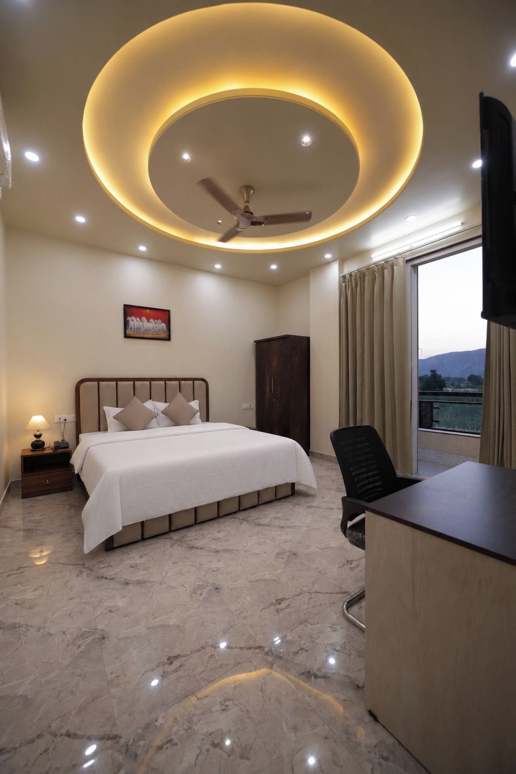 A hotel room with a bed, a desk, a chair, a ceiling fan, and a window with curtains.