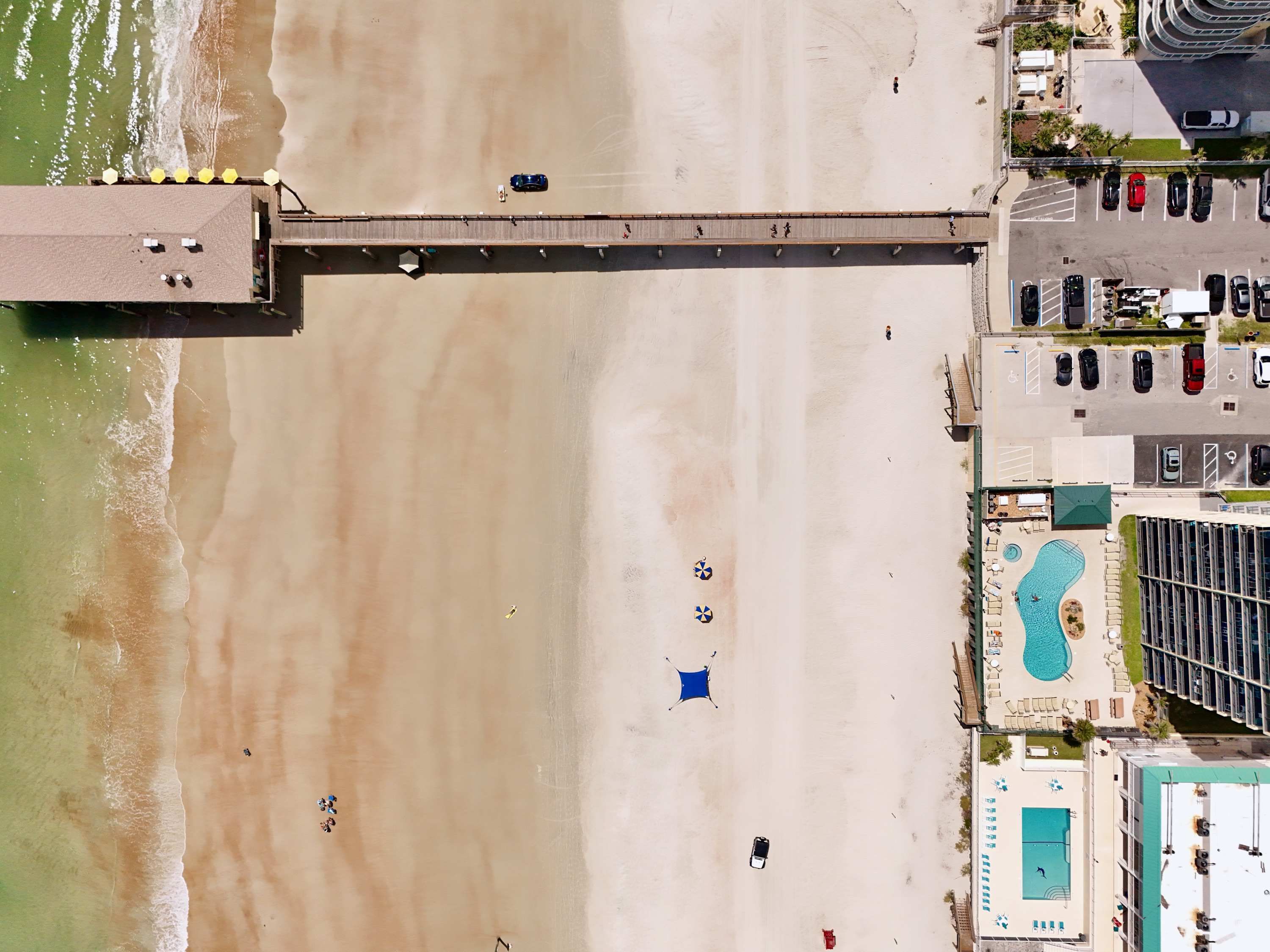 An aerial view of a beachside property with a pier, a swimming pool, and a parking area.