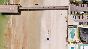 An aerial view of a beachside property with a pier, a swimming pool, and a parking area.