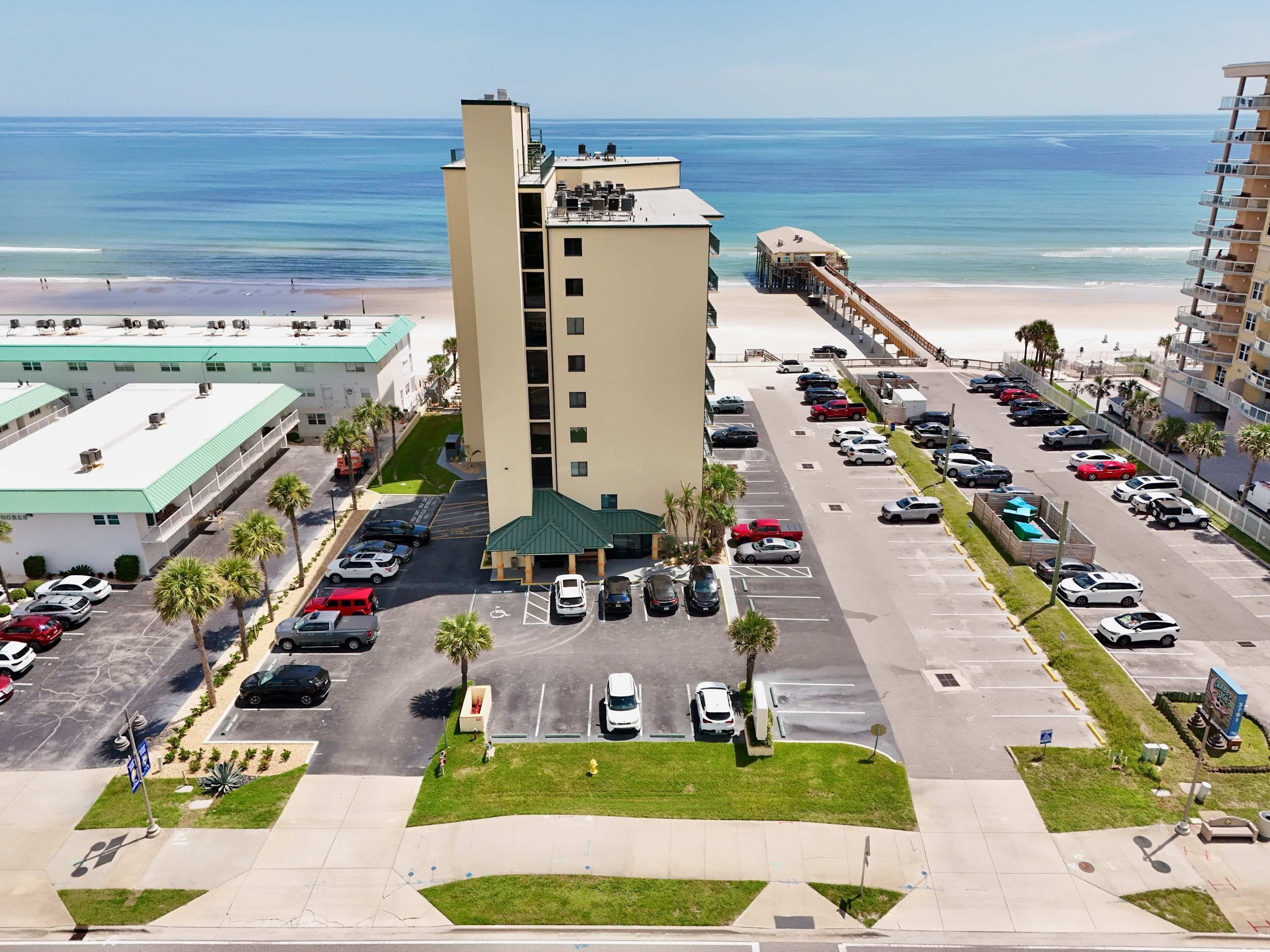 A hotel with a parking lot, a beach view, and a pool area.