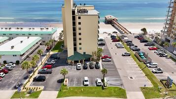 A hotel with a parking lot, a beach view, and a pool area.