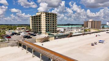 A beachfront hotel with multiple floors, a parking lot, and a boardwalk leading to the beach.