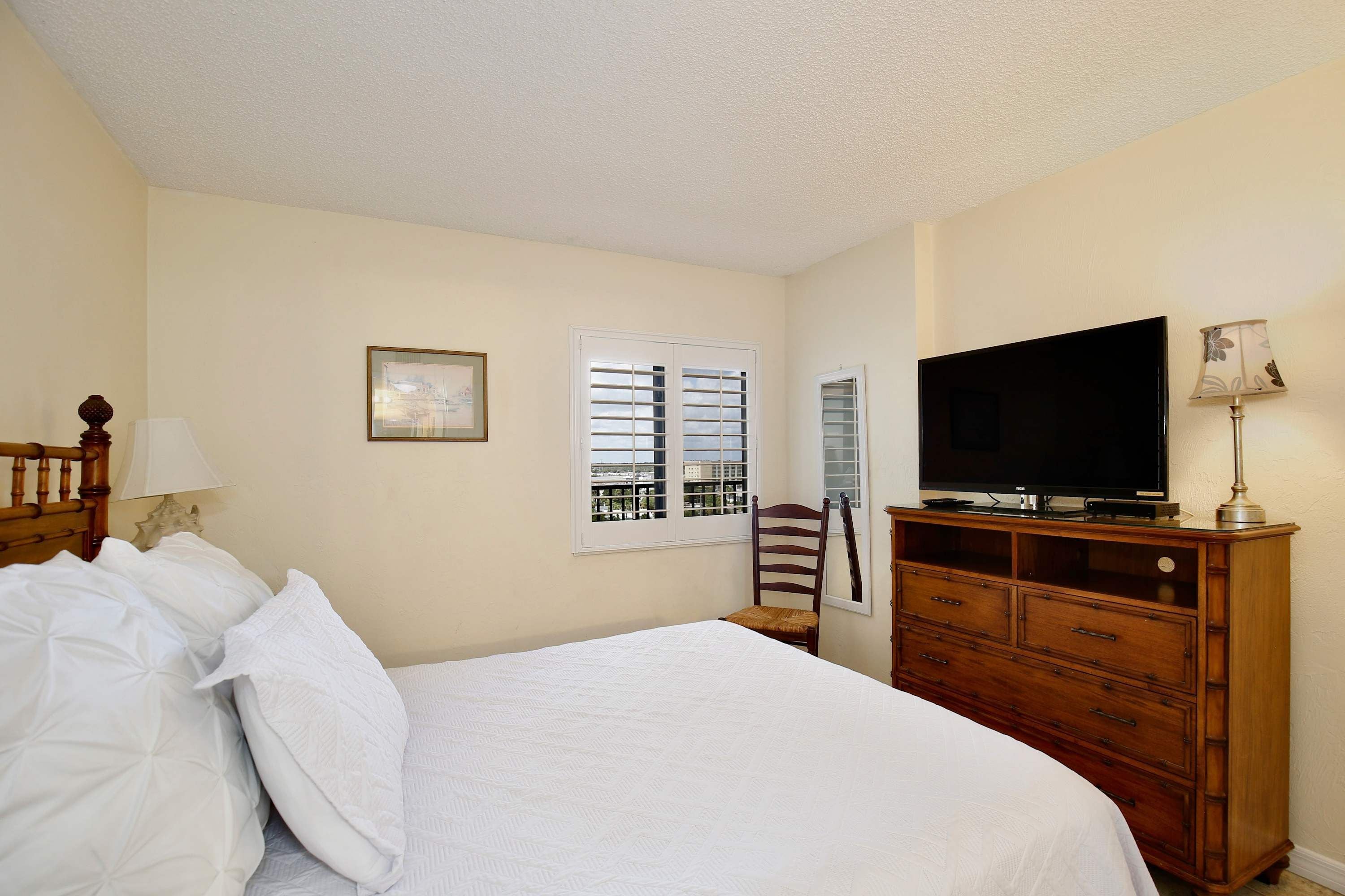 Habitación de hotel con cama, televisión, cómoda y ventana con persianas.