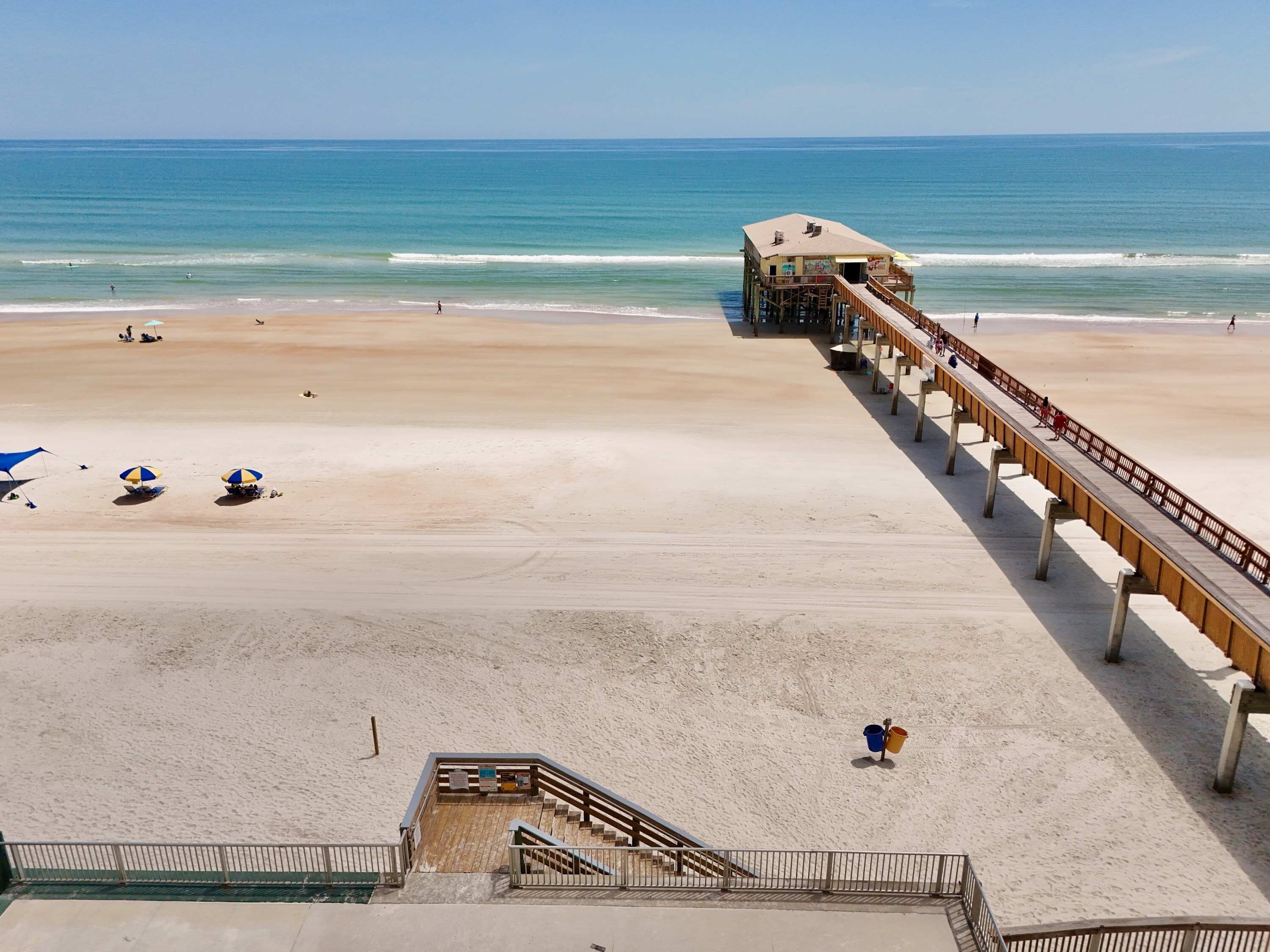 A beach with a wooden pier extending into the ocean, a sandy beach, and a few umbrellas.