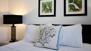 Una cama bien hecha con dos almohadas, una lámpara y dos cuadros en la pared.