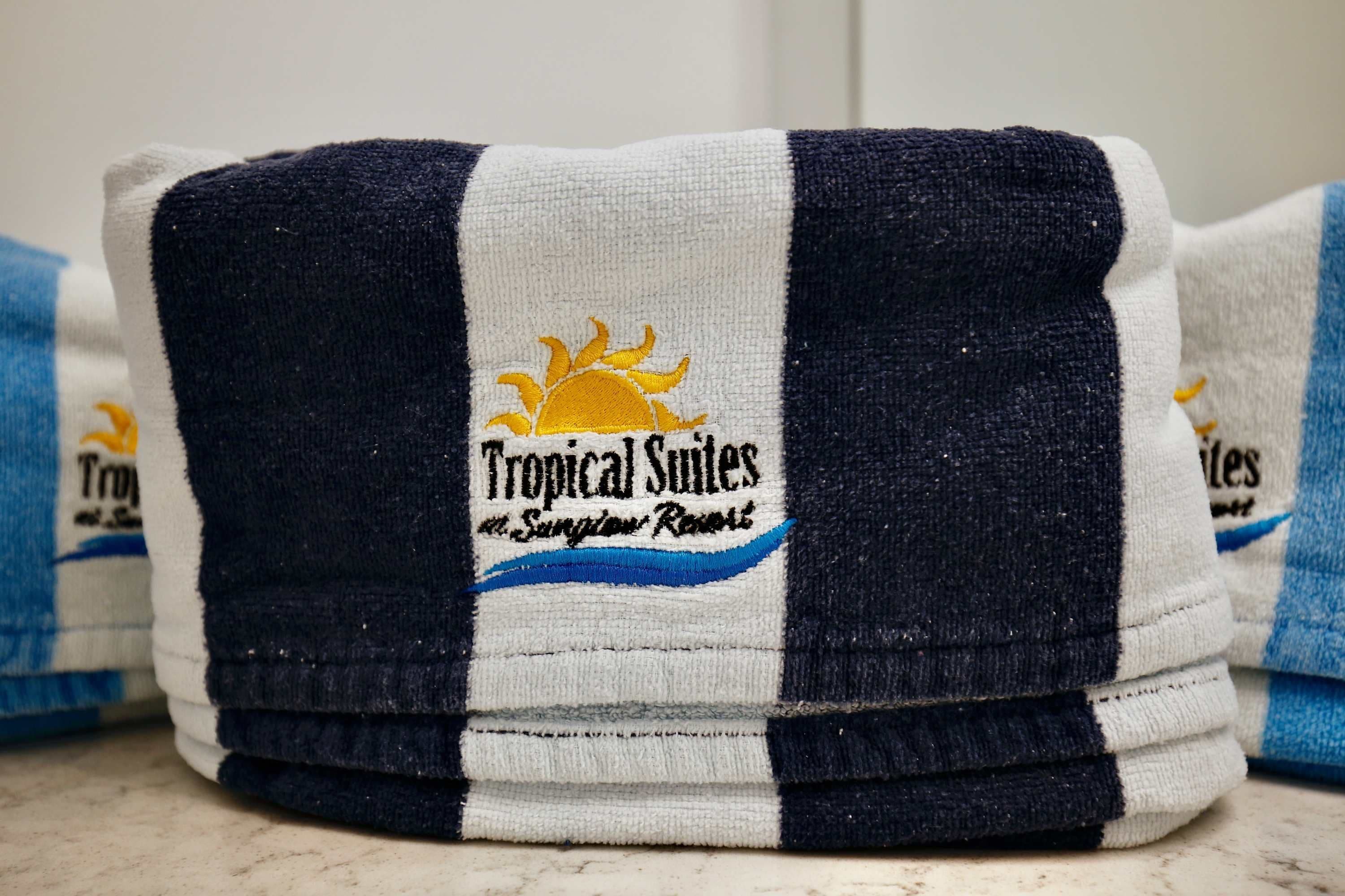 Une pile de serviettes ornées d’un logo et d’une inscription indiquant qu’elles proviennent de l’établissement « Tropical Suites ».