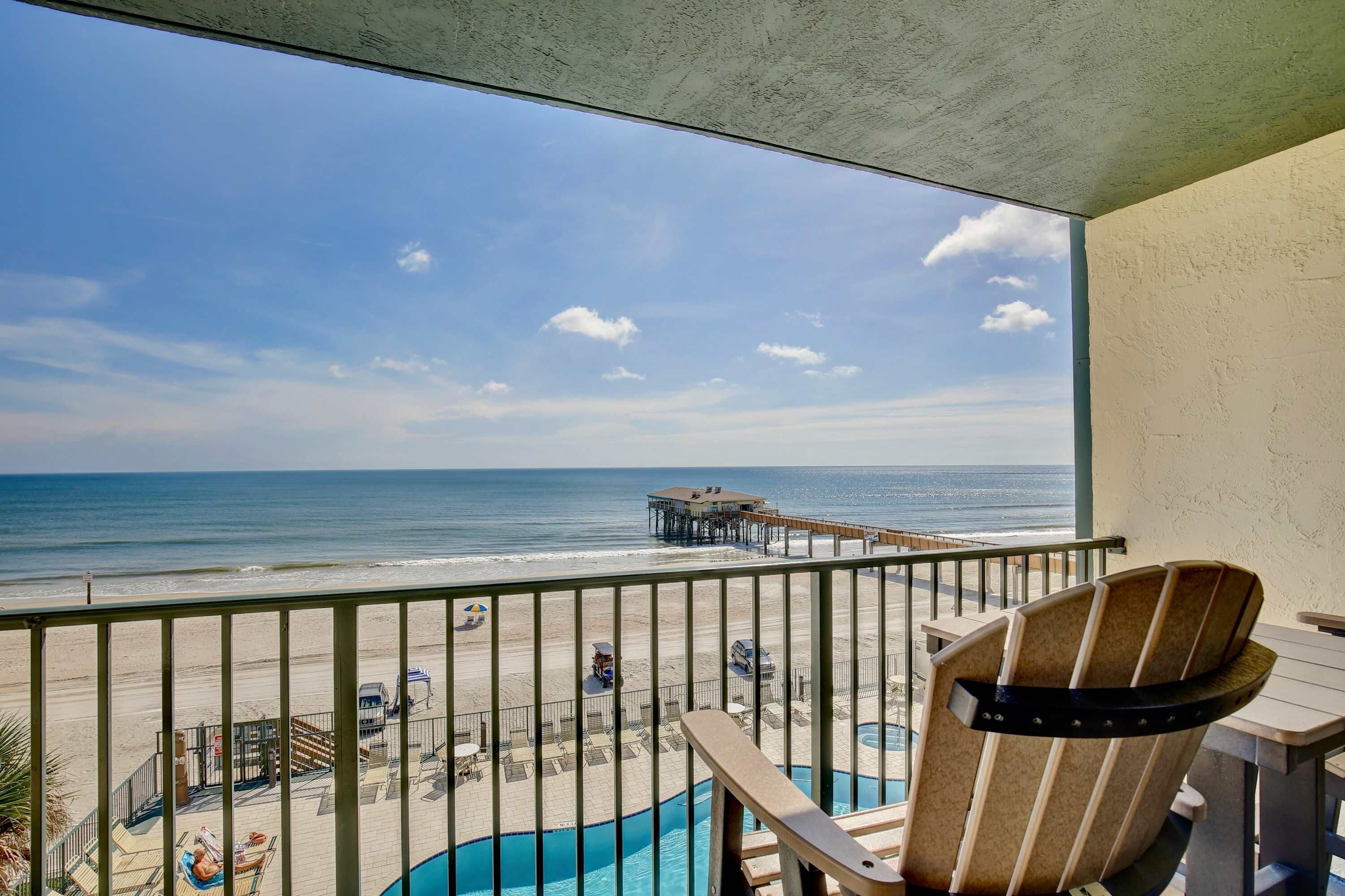 A balcony with a view of the beach, a pool, and a pier.