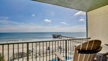 A balcony with a view of the beach, a pool, and a pier.