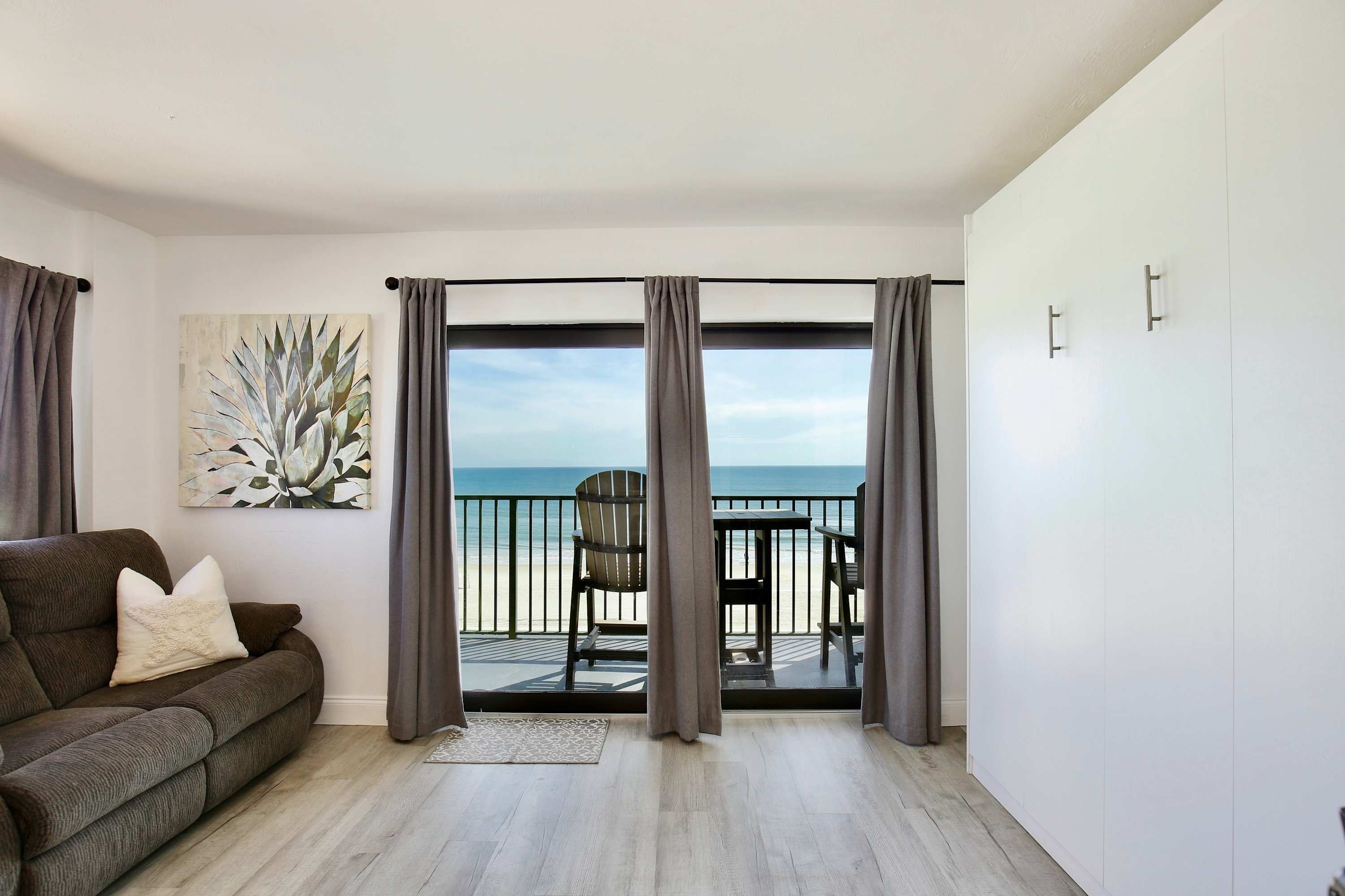 Una habitación con balcón con vistas al mar, un sofá y un cuadro.