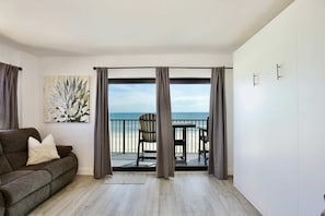Una habitació amb un balcó que dona al mar, un sofà i un quadre.