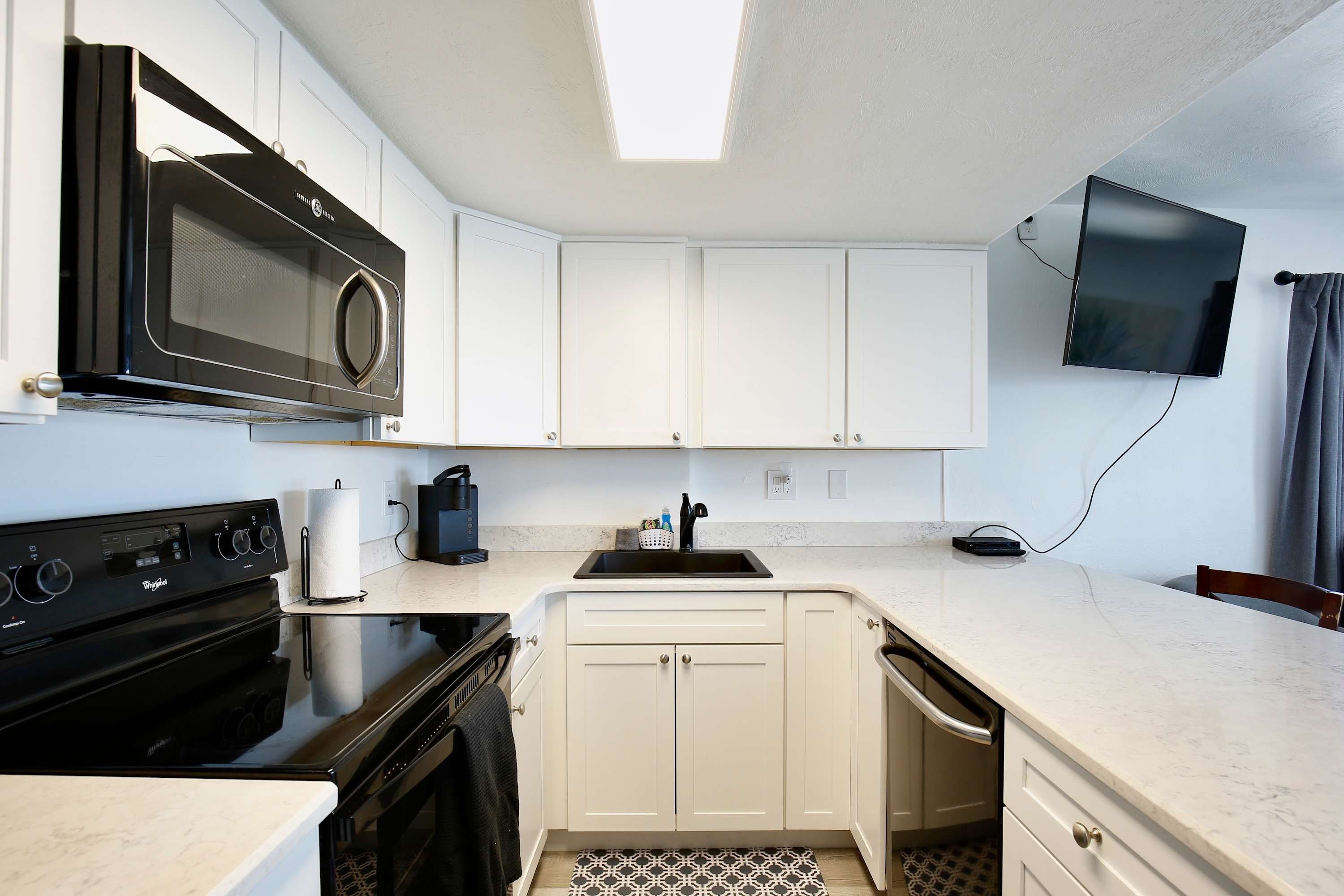 Une cuisine compacte équipée d’un four à micro-ondes, d’une cuisinière, d’un évier et d’un téléviseur à écran plat fixé au mur.