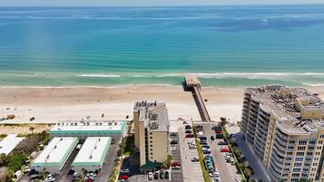 A coastal hotel with a parking lot, a beach, and a pier extending into the ocean.