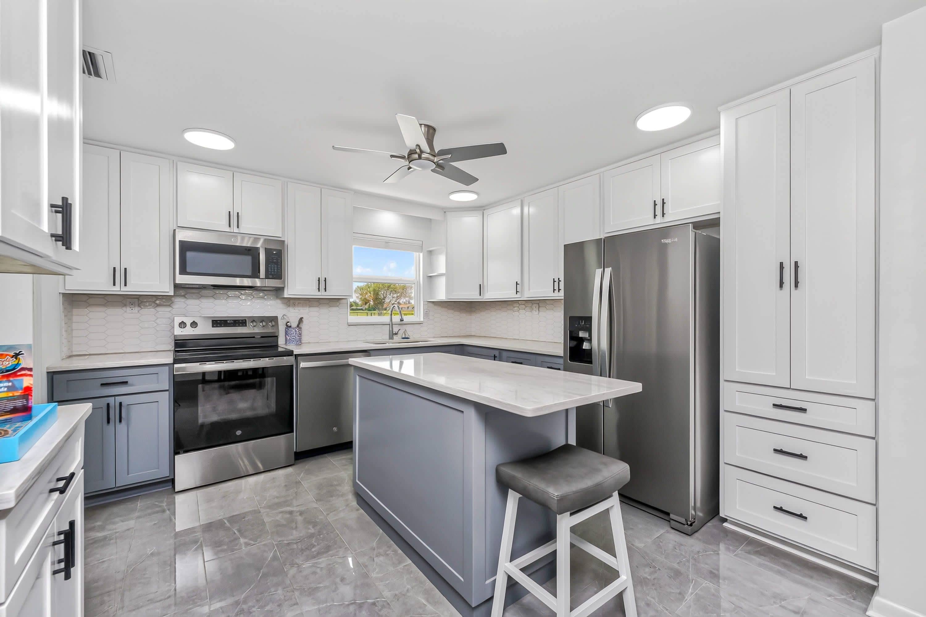 A modern kitchen with white cabinets, stainless steel appliances, a central island, and a ceiling fan.