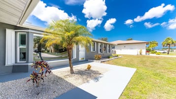 Une maison moderne à deux étages, dotée d’un patio couvert, d’un palmier et d’une pelouse bien entretenue.