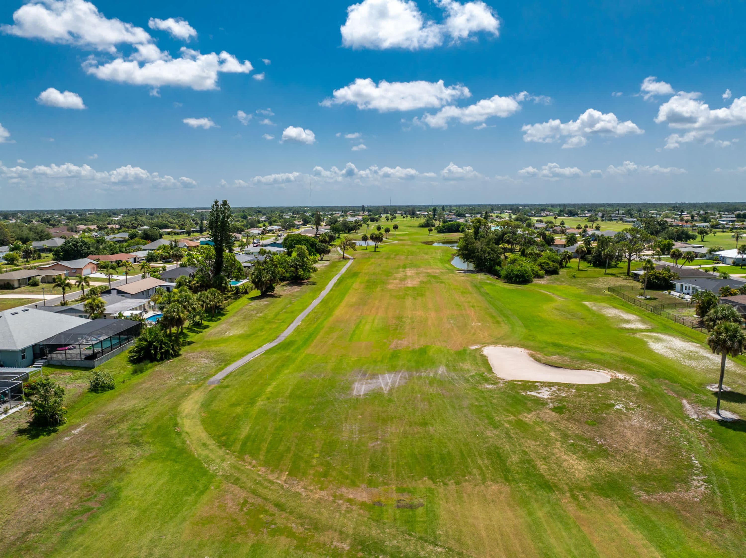 Un campo de golf bajo un cielo despejado, rodeado de viviendas y árboles.