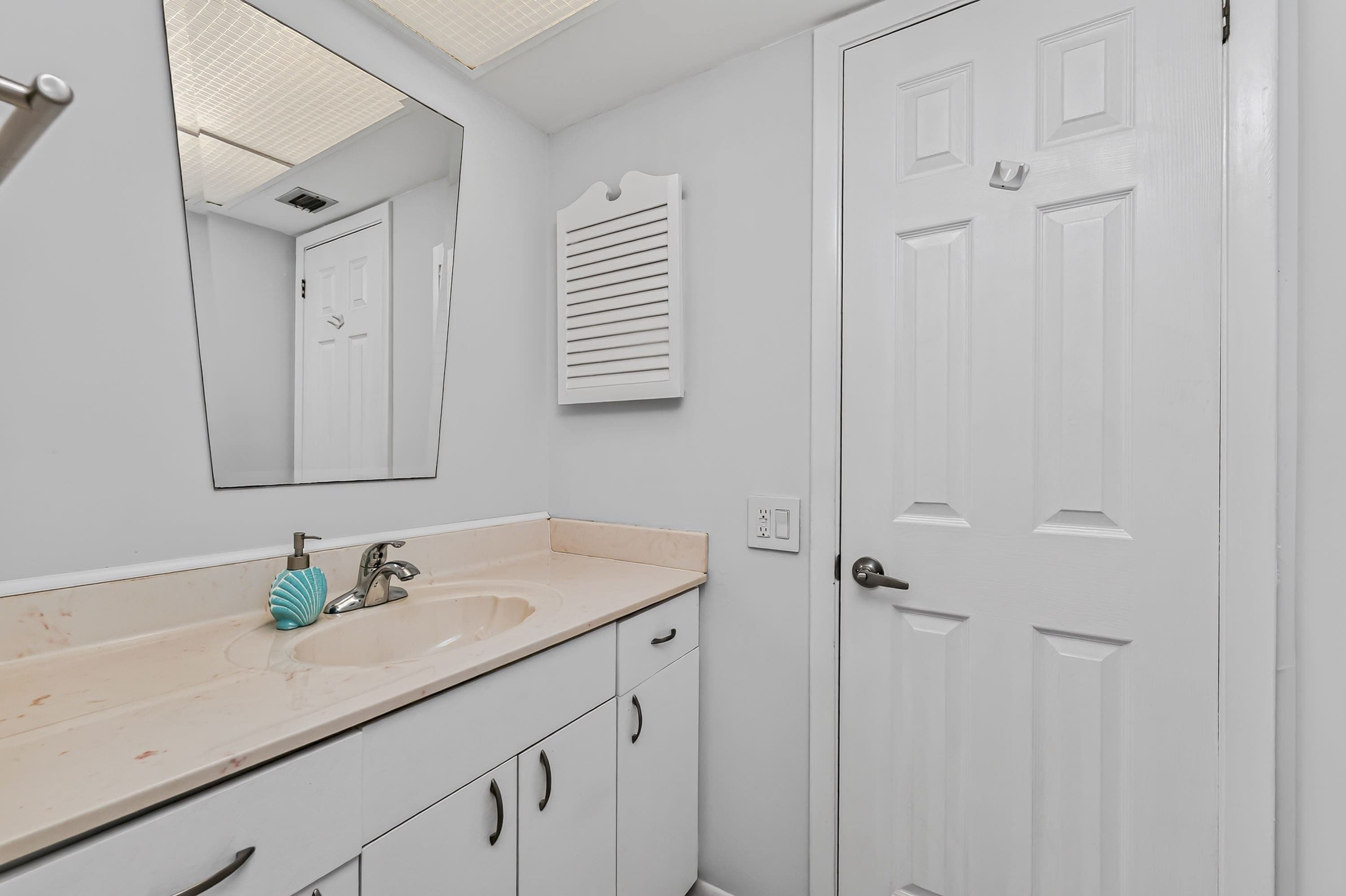 Une salle de bain avec un lavabo blanc, un miroir, un porte-serviettes et une porte.