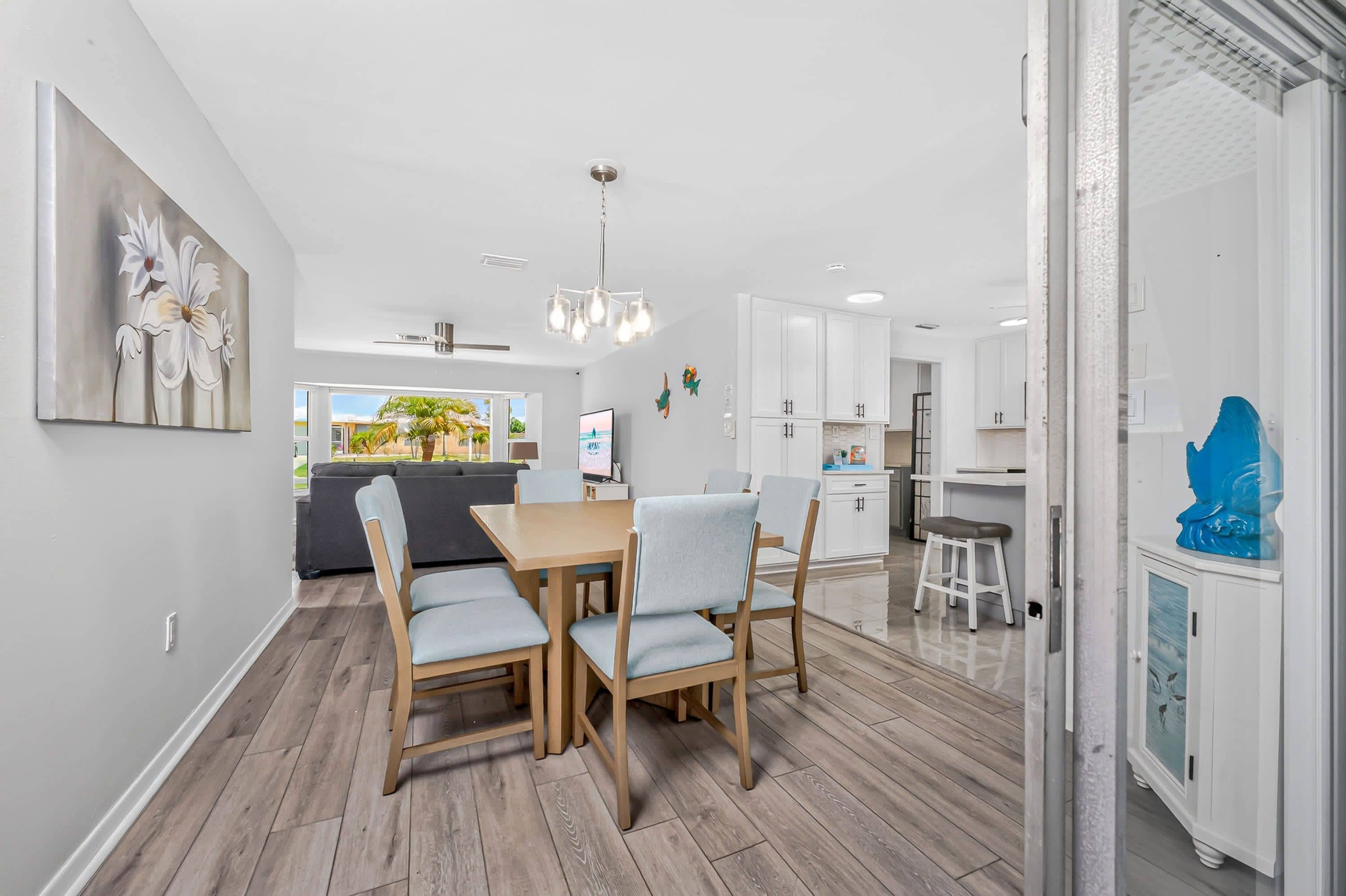 A modern kitchen with white cabinets, a dining area with a wooden table and chairs, and a view of the outdoors through the window.
