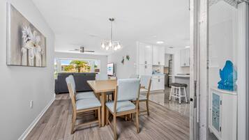 A modern kitchen with white cabinets, a dining area with a wooden table and chairs, and a view of the outdoors through the window.