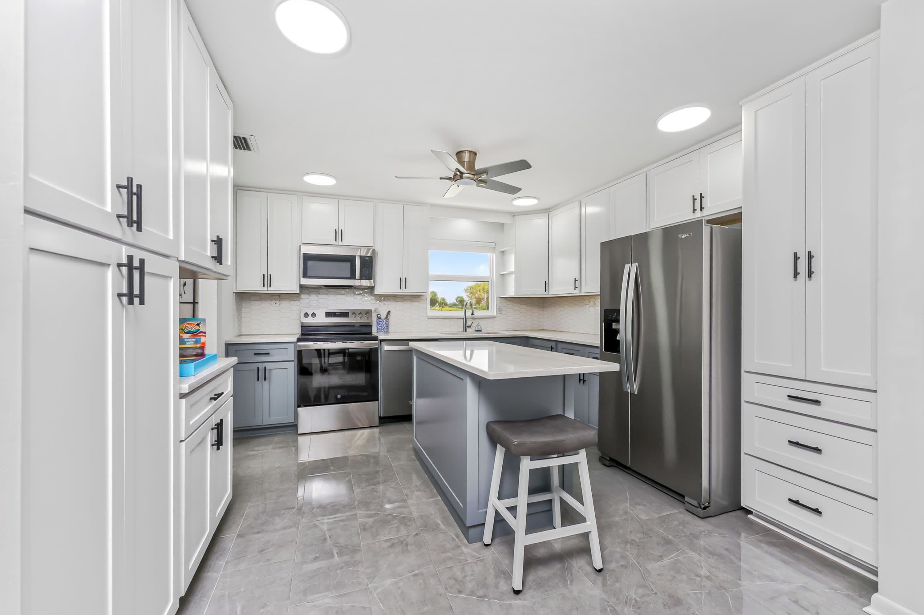A modern kitchen with white cabinetry, stainless steel appliances, a central island, and a ceiling fan.