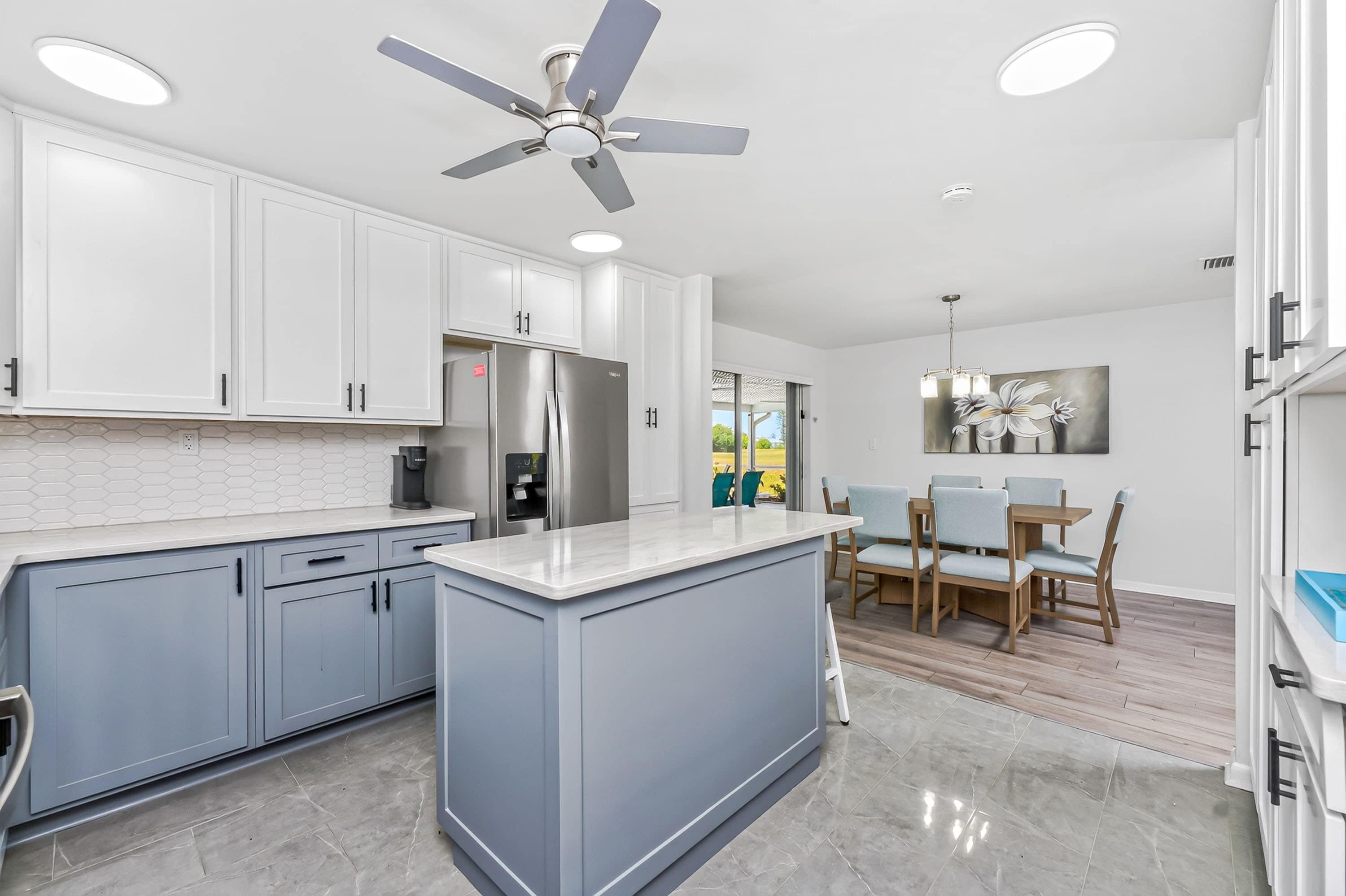 A modern kitchen with white cabinets, a stainless steel refrigerator, a built-in island, and a ceiling fan.