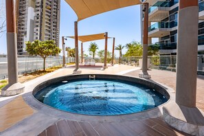 A swimming pool area with a hot tub, surrounded by palm trees and modern buildings. - Stayshort - Studio With Best Skyline View in JVT for 2 (Dubai)