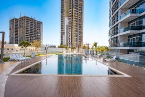 A swimming pool with sun loungers and a view of surrounding high-rise buildings. - Stayshort - Studio With Best Skyline View in JVT for 2 (Dubai)