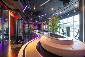 A modern gym interior with exercise equipment, a curved seating area, and large windows. - Stayshort - Studio With Best Skyline View in JVT for 2 (Dubai)