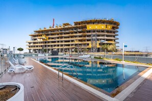 A multi-story building under construction with a swimming pool and lounge chairs. - Stayshort - Studio With Best Skyline View in JVT for 2 (Dubai)