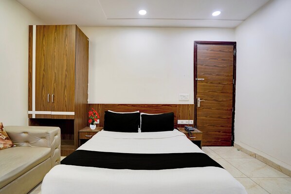 Habitación de hotel con una cama, un armario de madera, una mesita de noche con un jarrón de flores y otra mesita de noche con un teléfono.