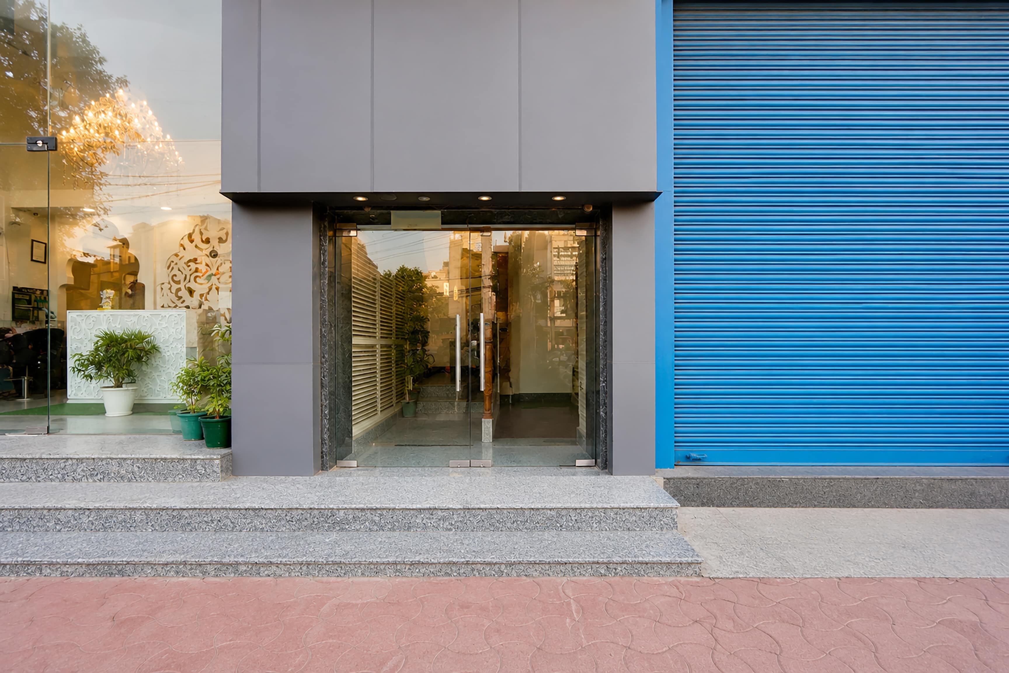 A modern building entrance with a glass door, potted plants, and a blue shutter door.